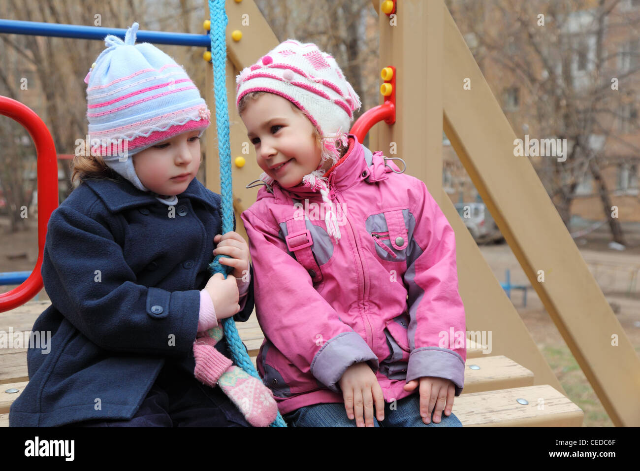 Two girls sit on playground, happy and sad Stock Photo