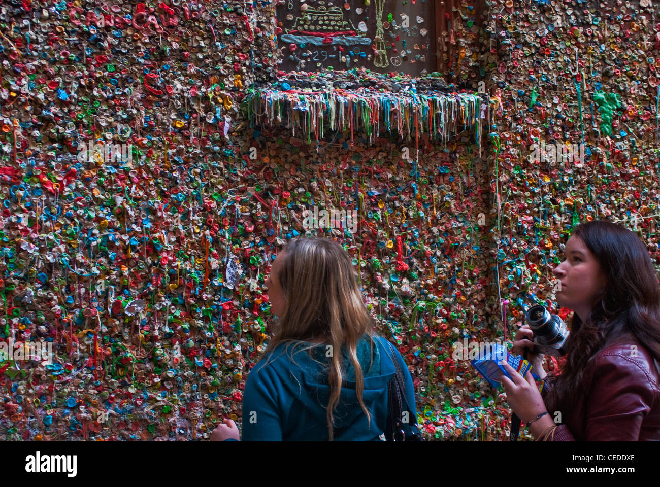 Two Women With A Camera And Bag Of Gum At Gum Wall Lower Level Pike Place Market Seattle WA Stock Photo