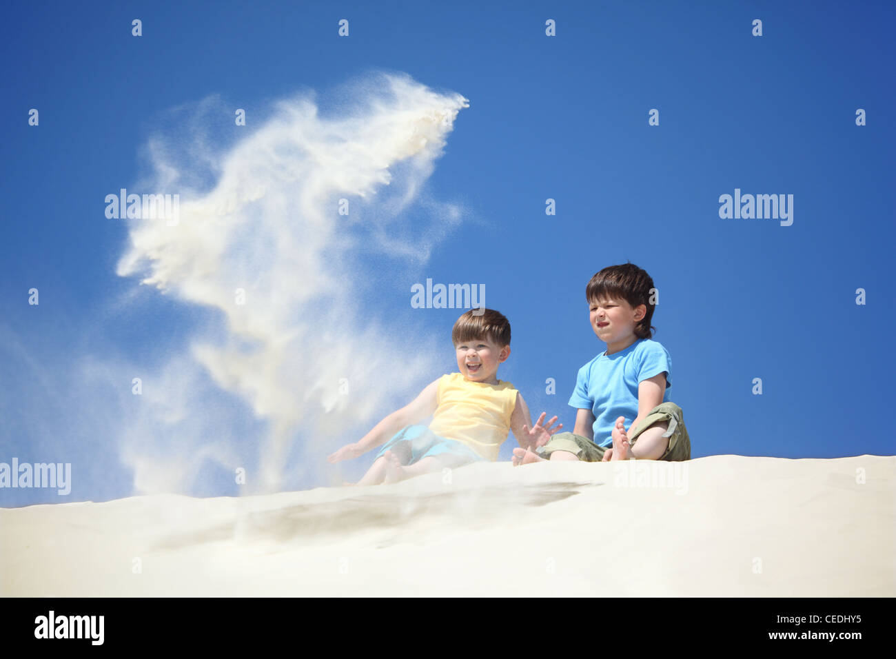 two boys sit on sand and scatter it Stock Photo