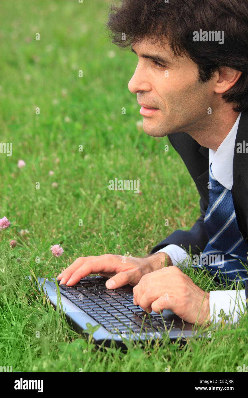 Businessman lying on the meadow and typing Stock Photo