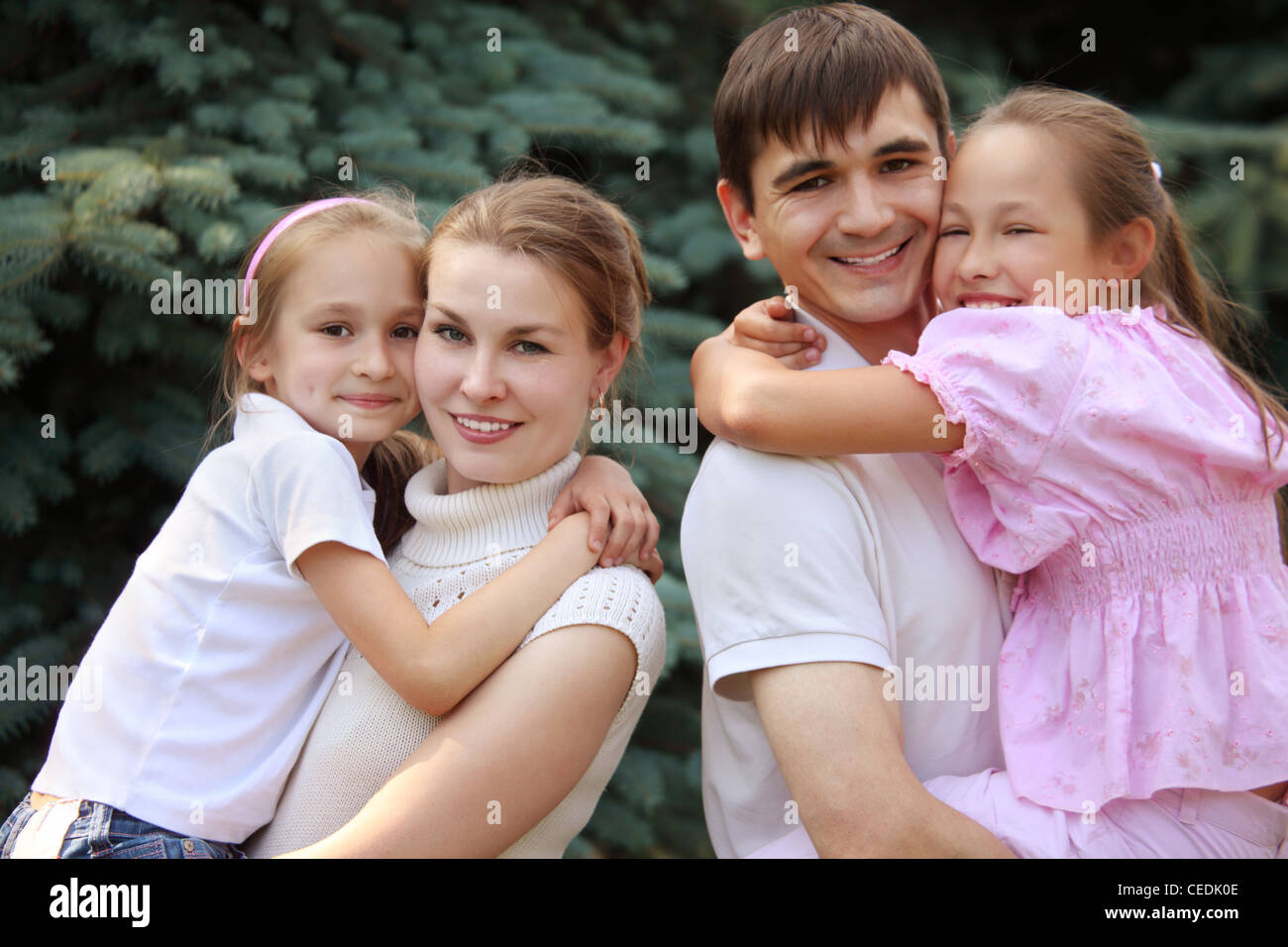 two parents hold children on hands on fir background Stock Photo