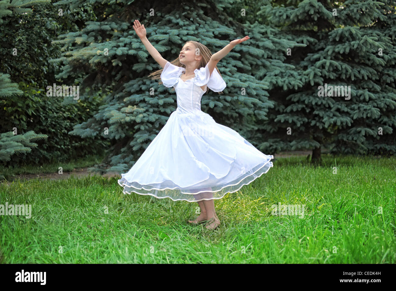girl in white dress dances on lawn with lifted hands Stock Photo - Alamy