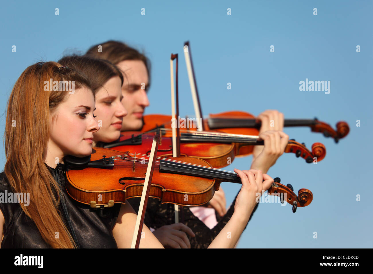 trio of violinists plays against sky Stock Photo