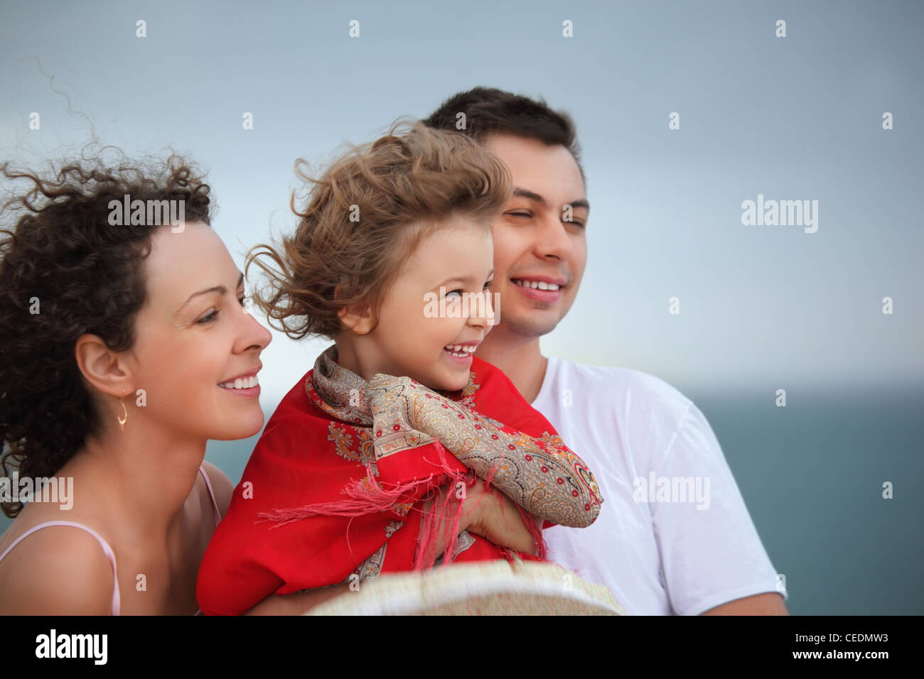 young man and beautiful woman protects little girl from wind on seacoast Stock Photo