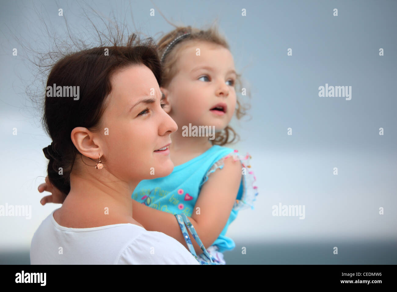 beautiful woman protects little girl from wind on seacoast Stock Photo