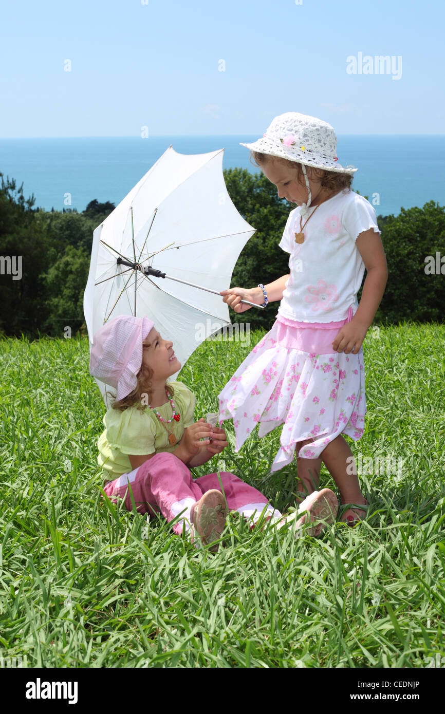 Two little girls with an umbrella on lawn near sea Stock Photo - Alamy