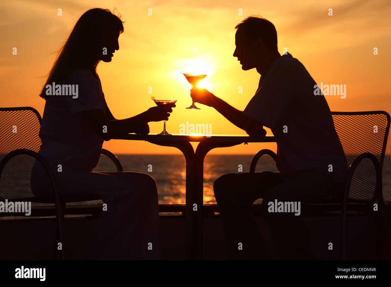 Female and man's silhouettes on sunset sit at table with two glasses outdoor Stock Photo