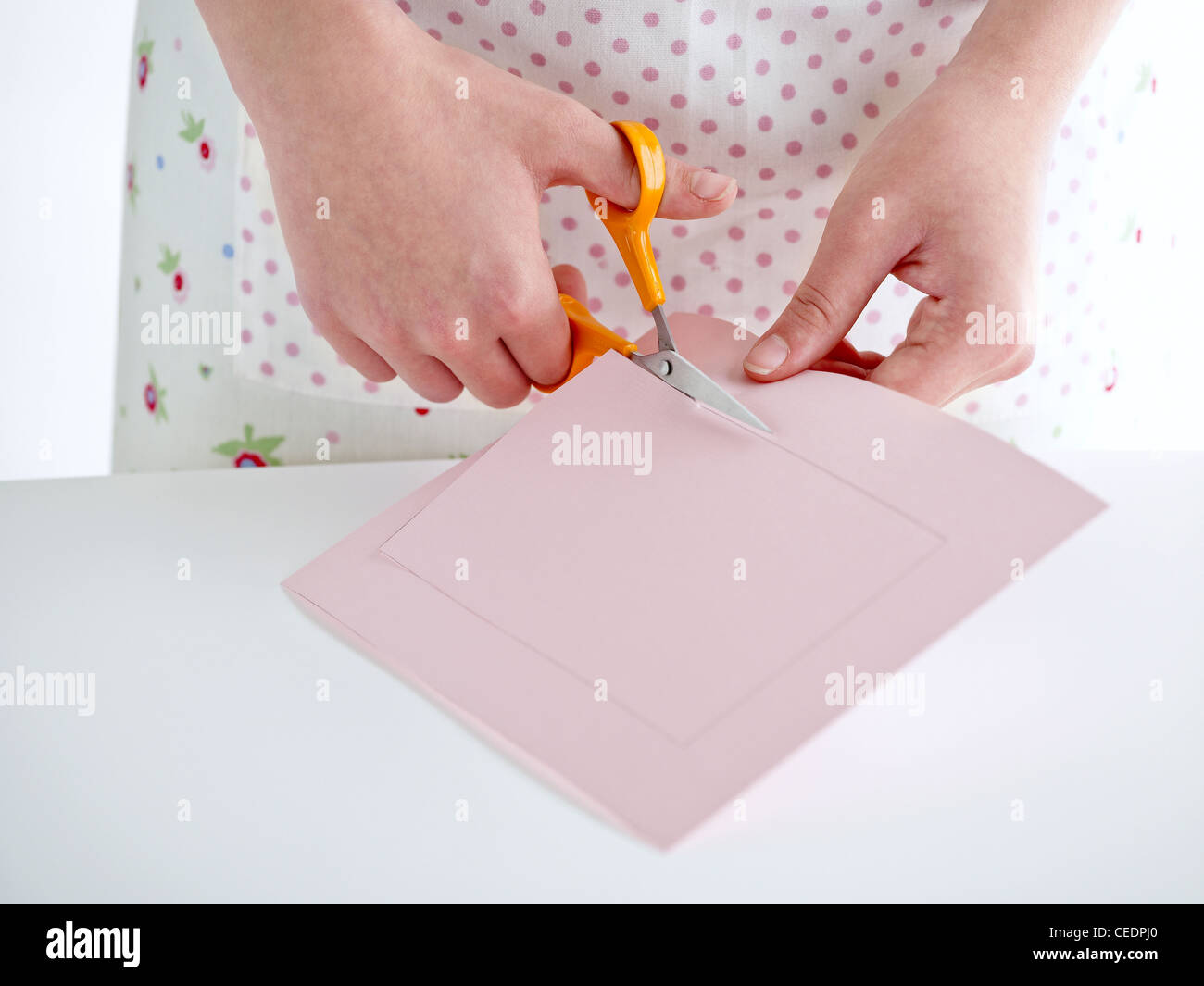 Girl using scissors and cutting a square on pink paper Stock Photo