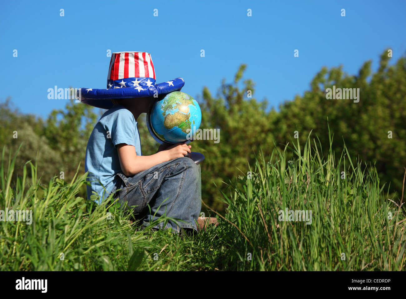 boy in big american flag hat sits on  grass and holds globe Stock Photo