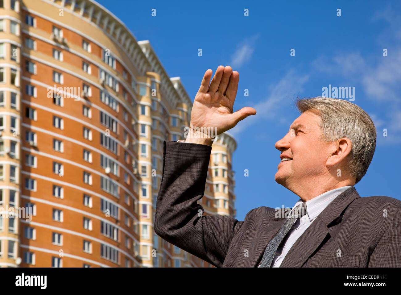 Senior man in suit at the new residental building with hand up Stock Photo