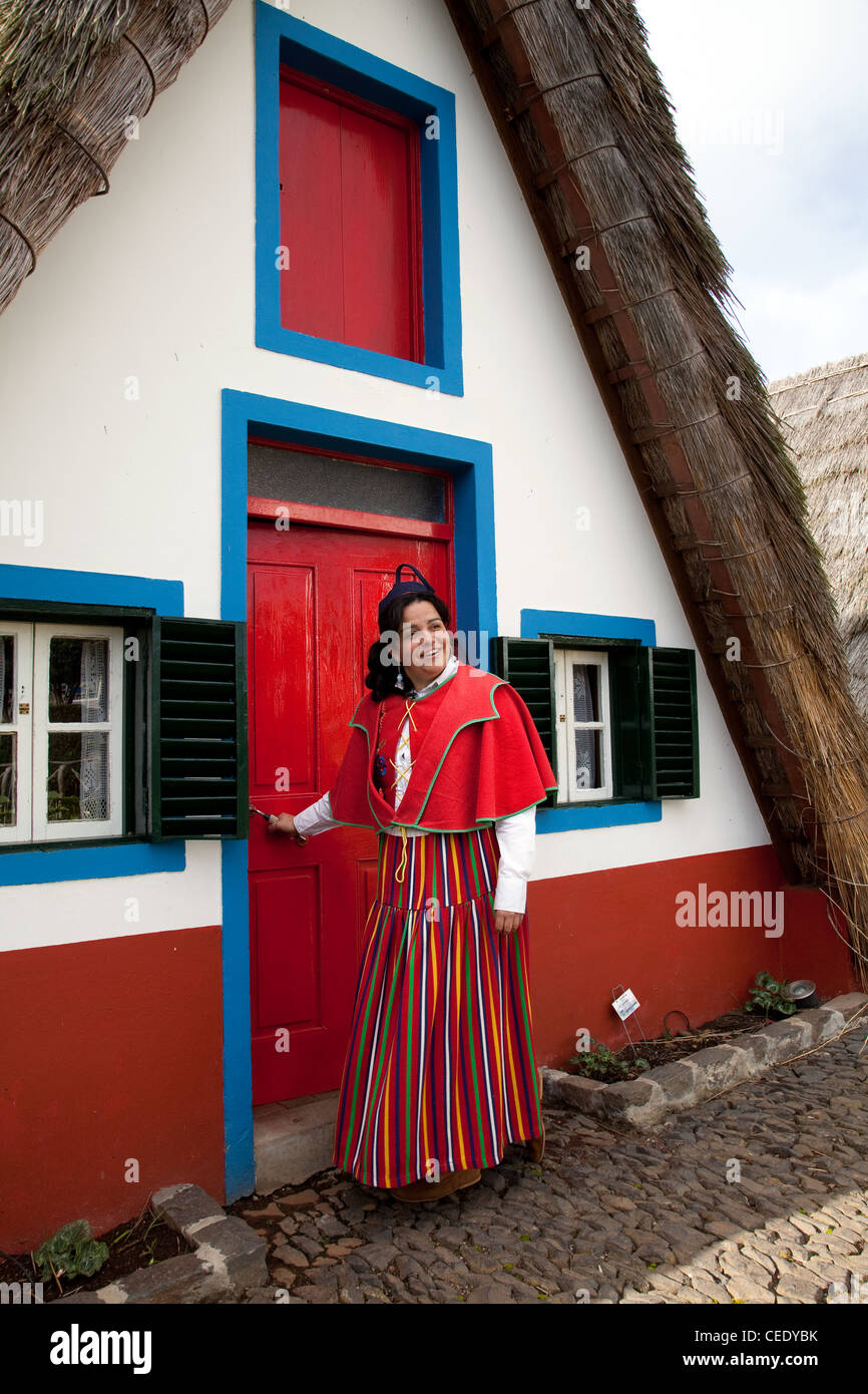 Traditional triangular A-framed Palheiro thatched Portuguese house. Woman dressed in Traditional costume of multi-coloured fabrics Santana, Madeira Stock Photo
