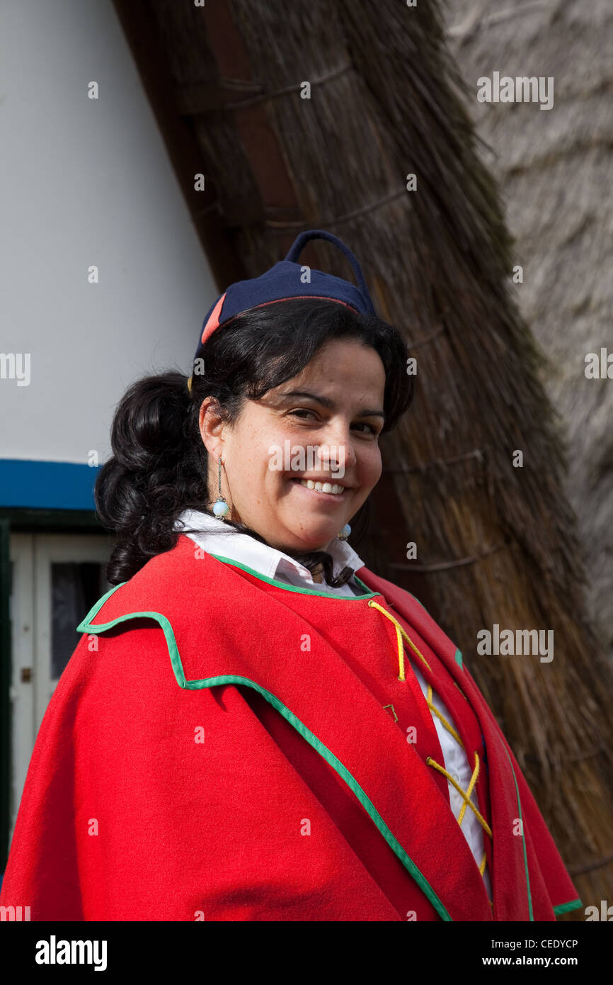 Traditional triangular A-framed Palheiro thatched Portuguese house. Woman dressed in Traditional costume of multi-coloured fabrics Santana, Madeira Stock Photo