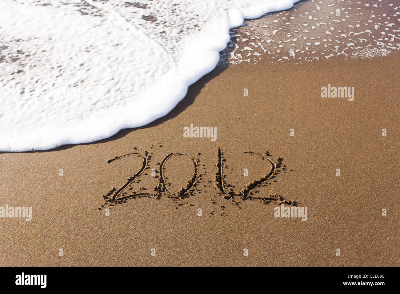 2012 written in sand on beach with sea waves starting to erase the word Stock Photo