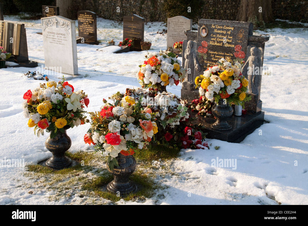 A grave with many flowers in memory, in winter snow, Suffolk UK Stock