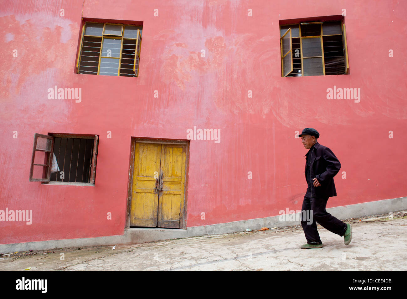 Traditional Chinese man walking passing a colourful pink house  with yellow door in Yuanyang China Asia Stock Photo