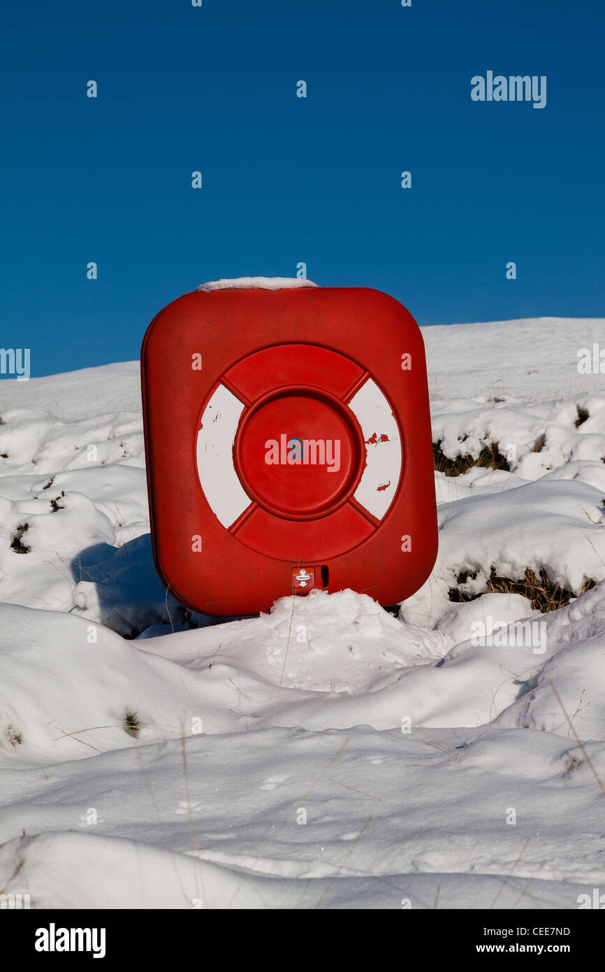 High and Dry - A bright red floatation life buoy sits buried in the snow next to a lake Stock Photo