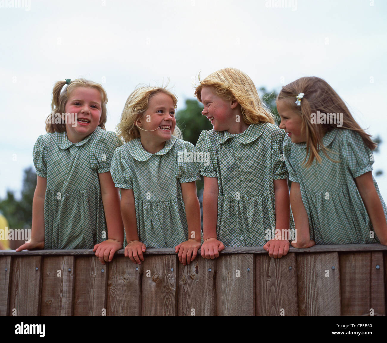 Primary school girls standing on fence, Surrey, England, United Kingdom Stock Photo