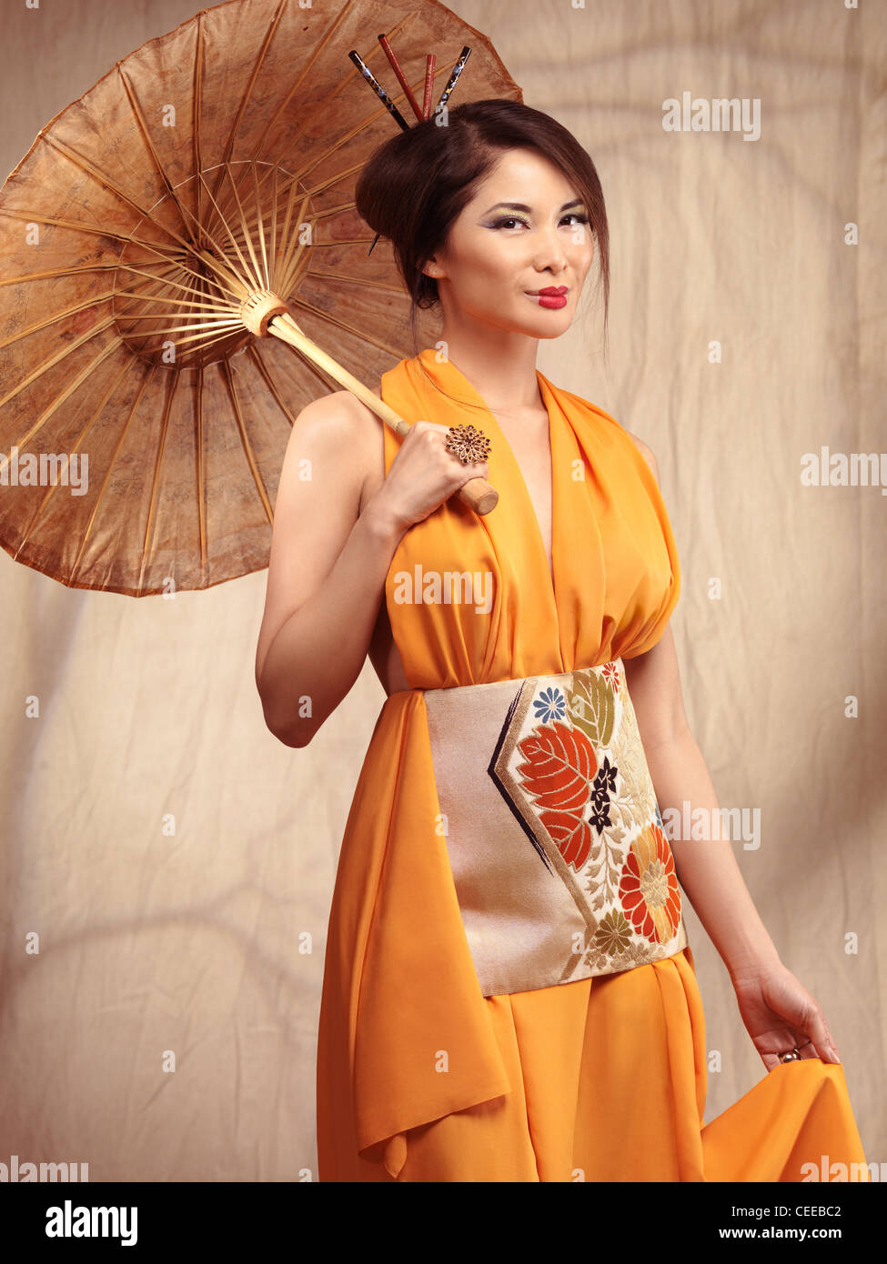 Beautiful asian woman wearing an orange dress stading with an umbrella in her hand Stock Photo