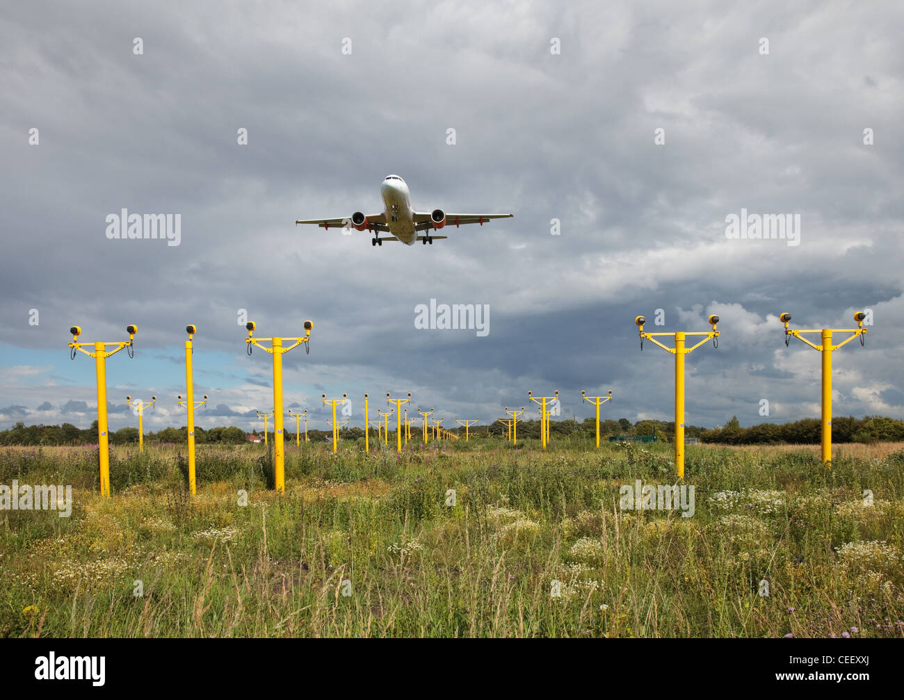 Plane flies low over landing lights on approach to the runway. Stock Photo