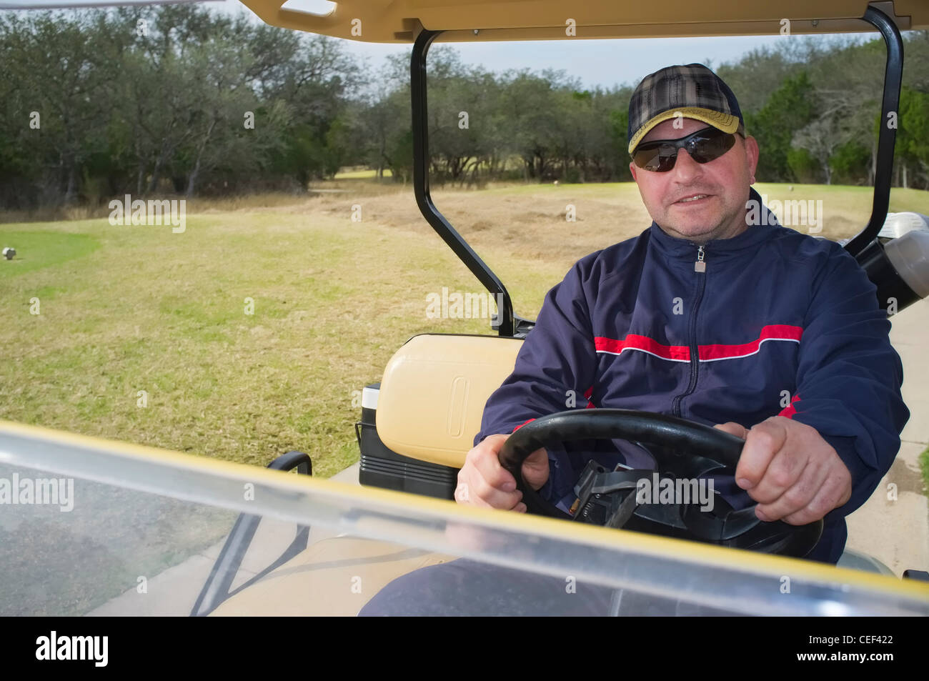 Middle aged male golfer in sweat suit riding a golf cart Stock Photo