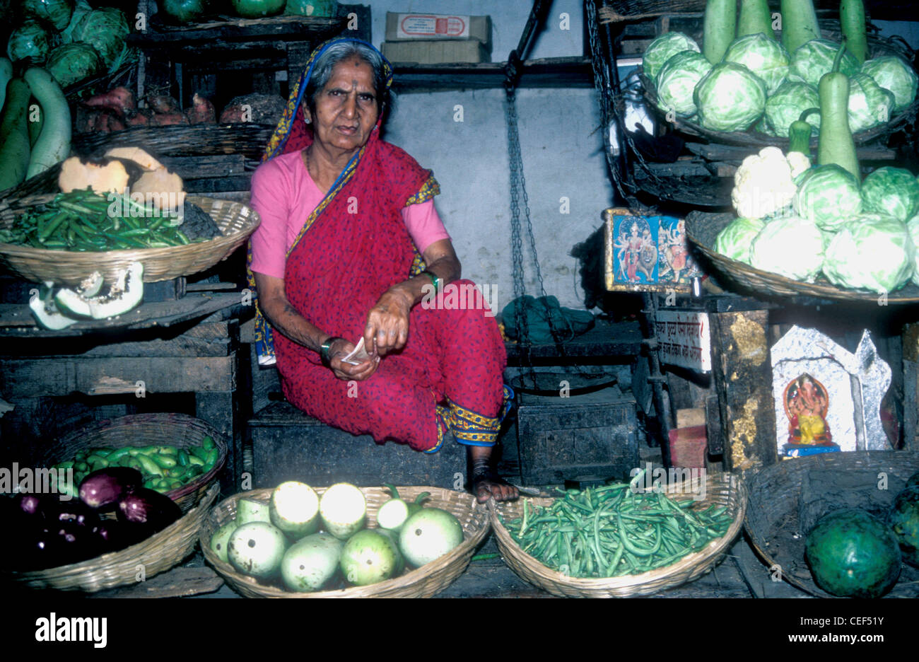 Woman trader in Crawford Market in Mumbai with photo of Ganesh and vegetables, 1975 Stock Photo