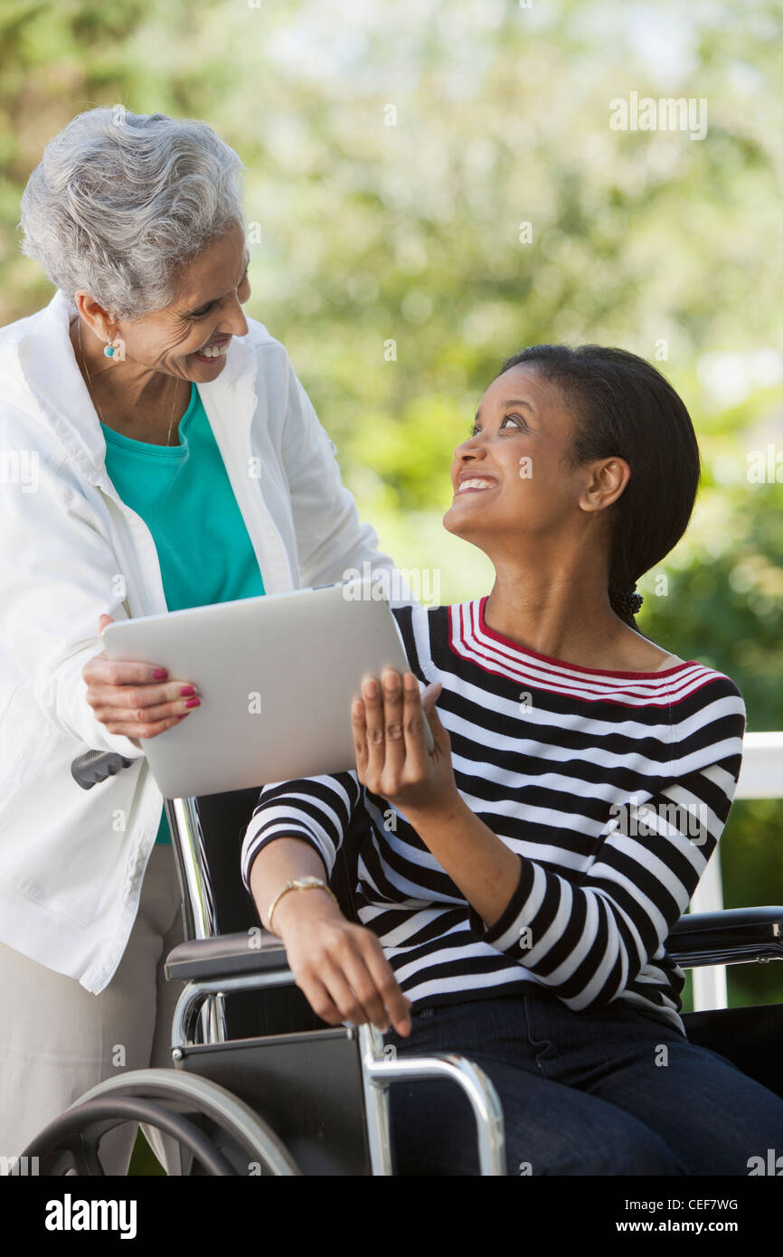 Disabled Woman in a wheelchair sharing a Digital Tablet with her mother Stock Photo