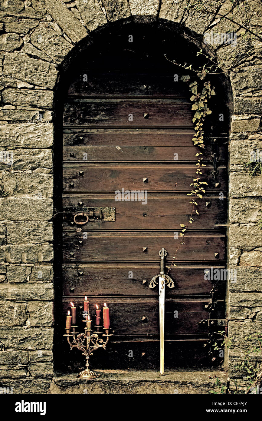 a candleholder and a sword in front of an old wooden door Stock Photo