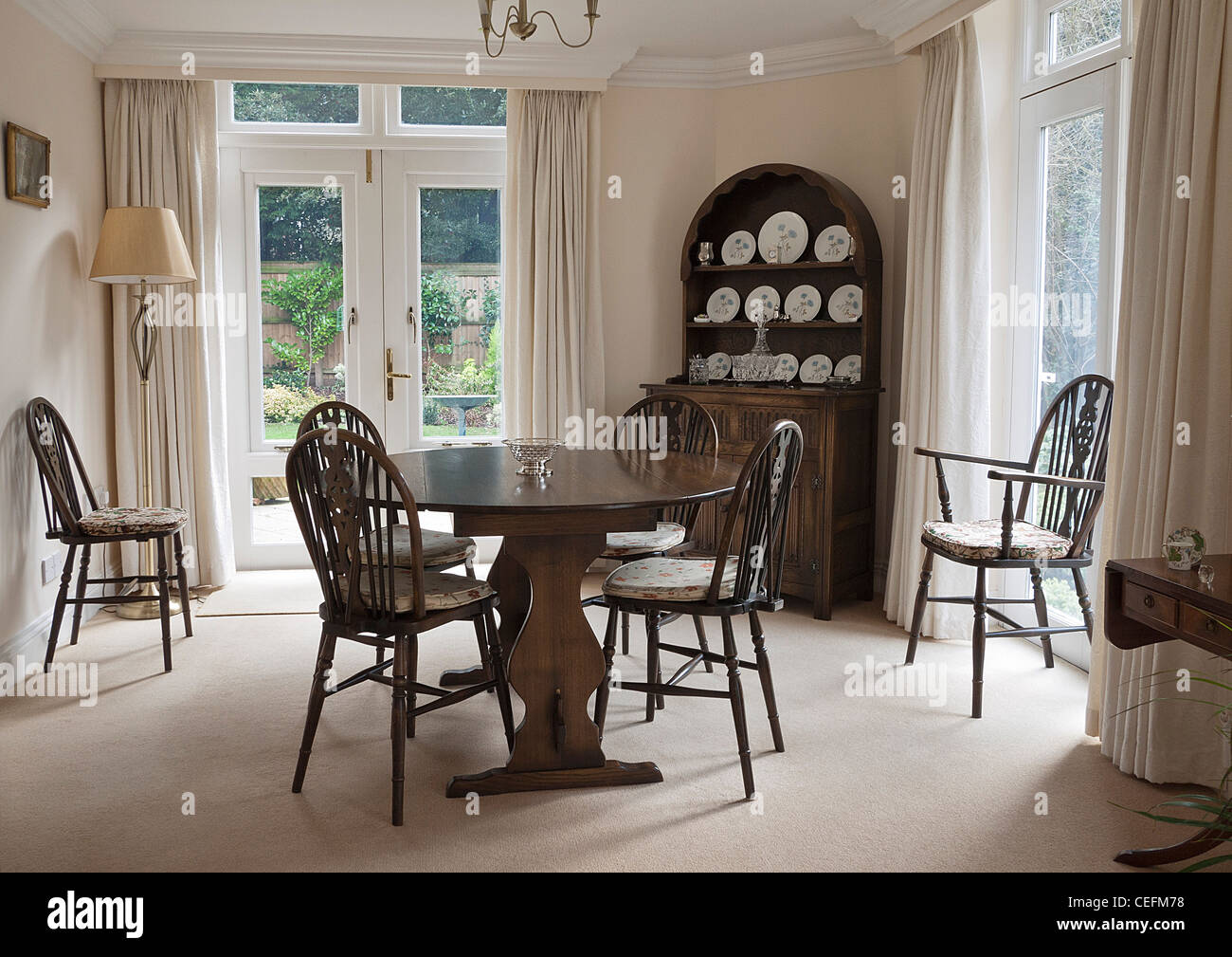 Traditional Dining Room with Dutch Dresser, table and chairs, curtains and French windows. UK. Stock Photo