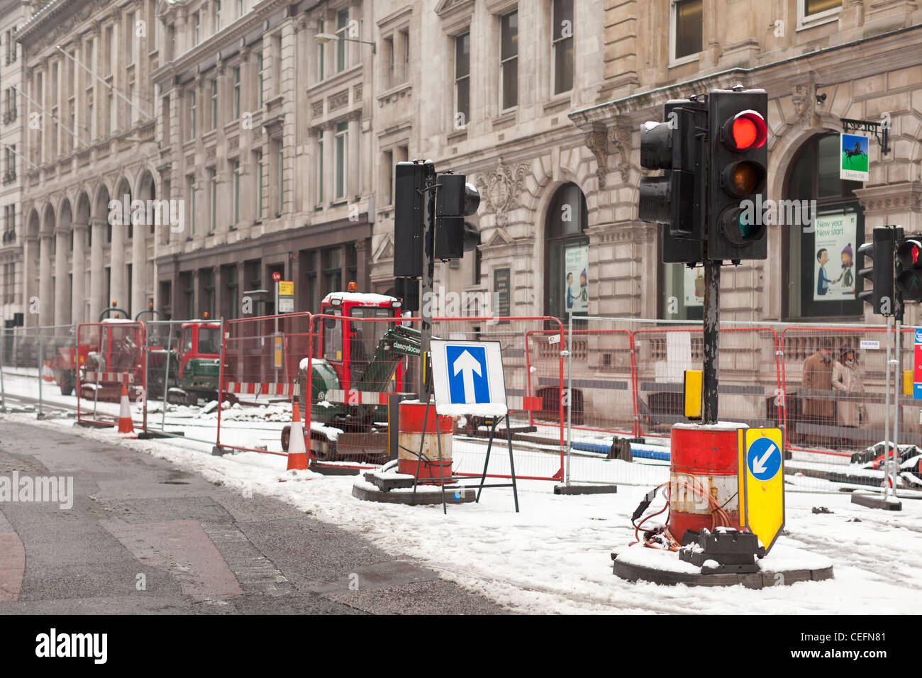 Red traffic light and closed lane at roadworks in winter snow in the city of London, UK Stock Photo