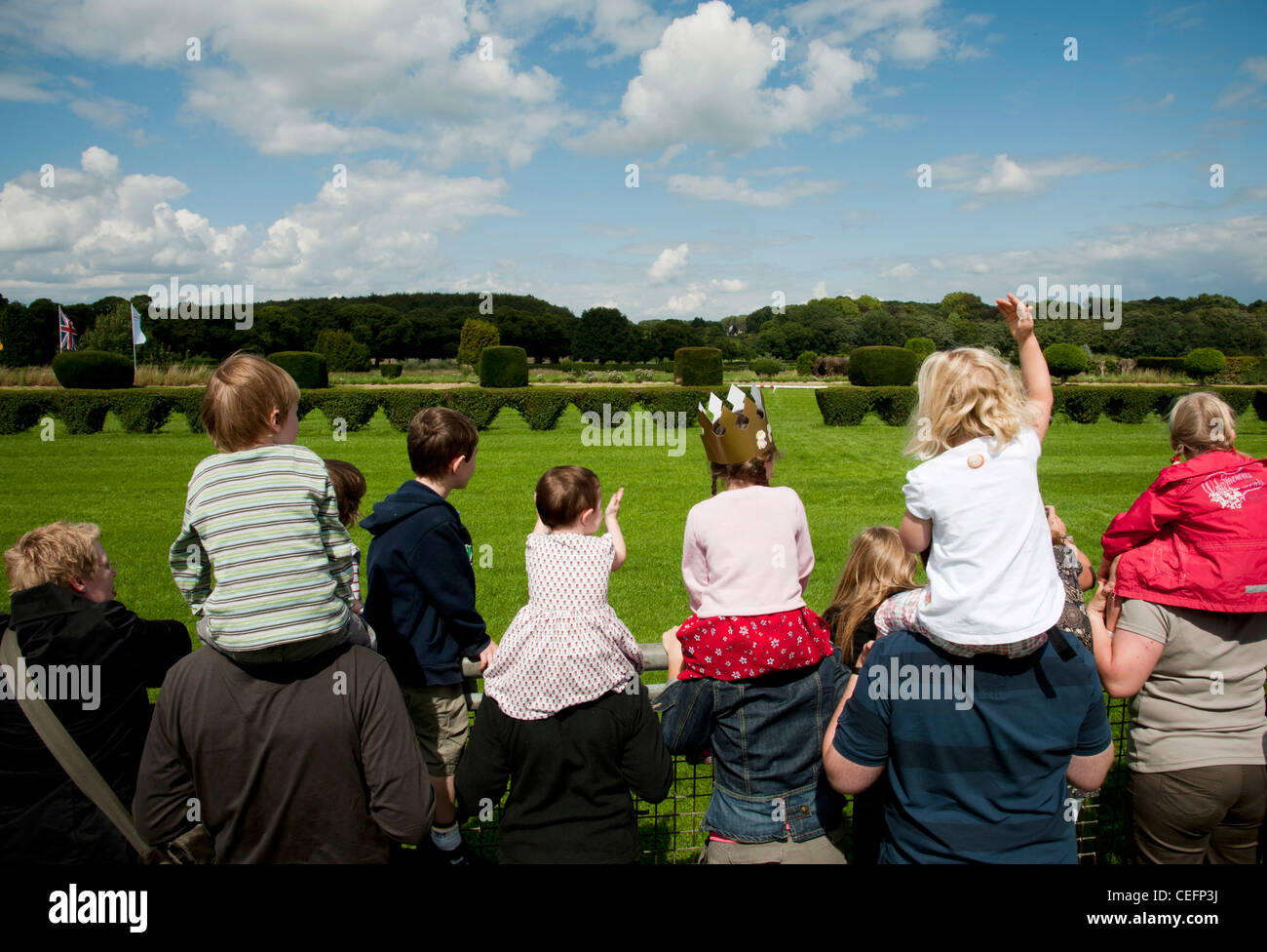 children sit on the shoulders of their parents and wave on empty racetrack during horse race Stock Photo