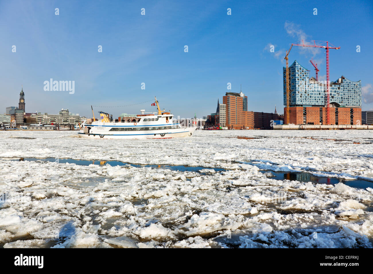 Hamburg and the frozen Elbe river from Saint Michaels church to the Elbphilharmonie construction site, tourist boat passing by Stock Photo