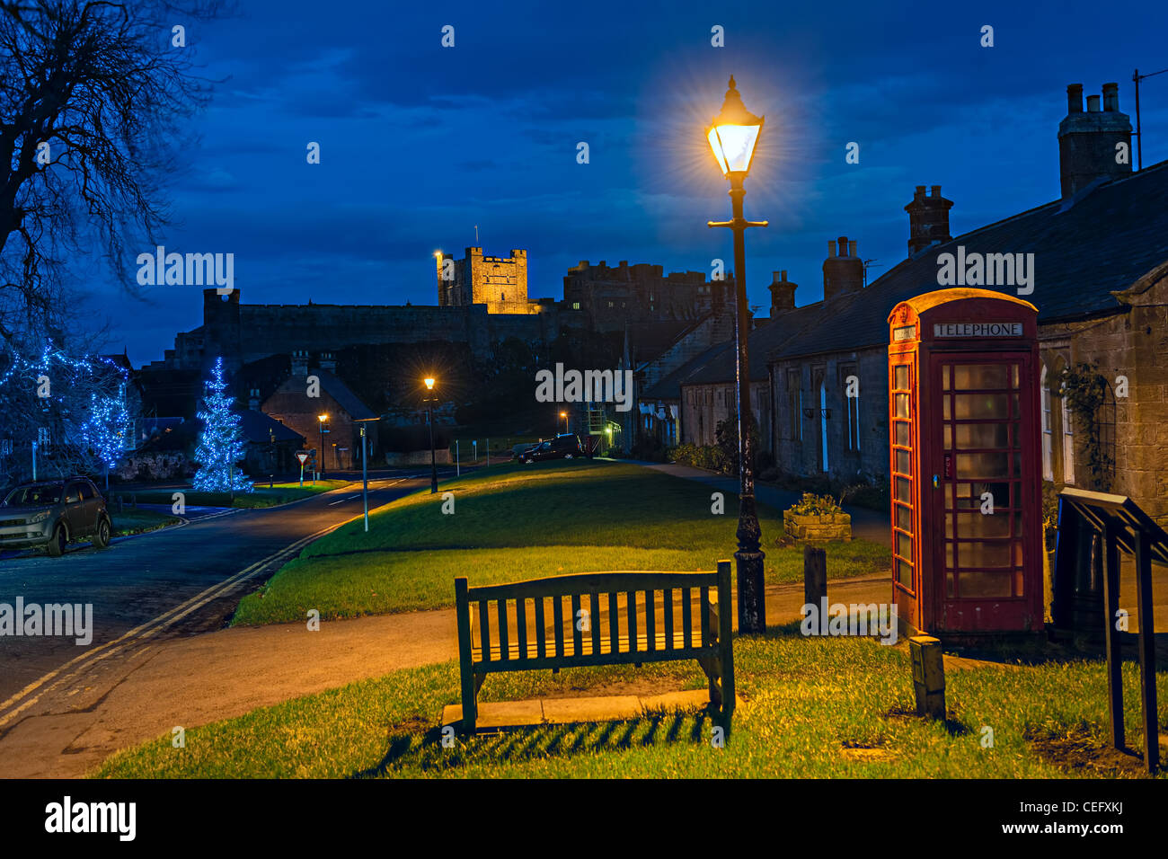 Bamburgh village, Northumberland, England, UK, at dusk, with Bamburgh Castle in the background, at Christmas Stock Photo