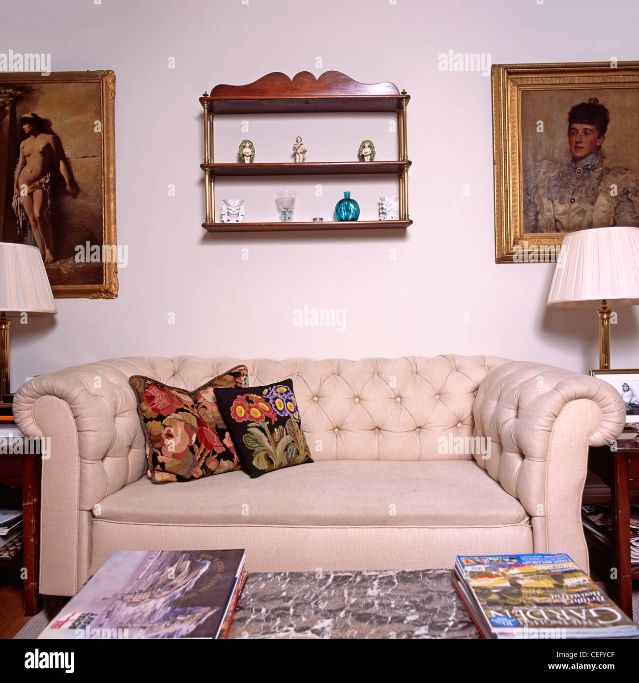 Floral tapestry cushions on cream Chesterfield sofa below antique shelves  in traditional living room Stock Photo - Alamy