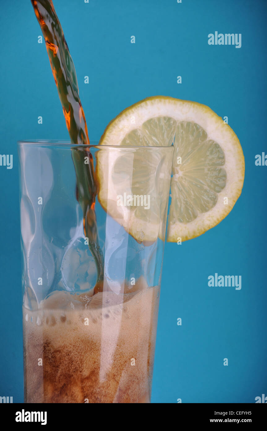 pouring soda into a glass with a lemon slice (blue background Stock