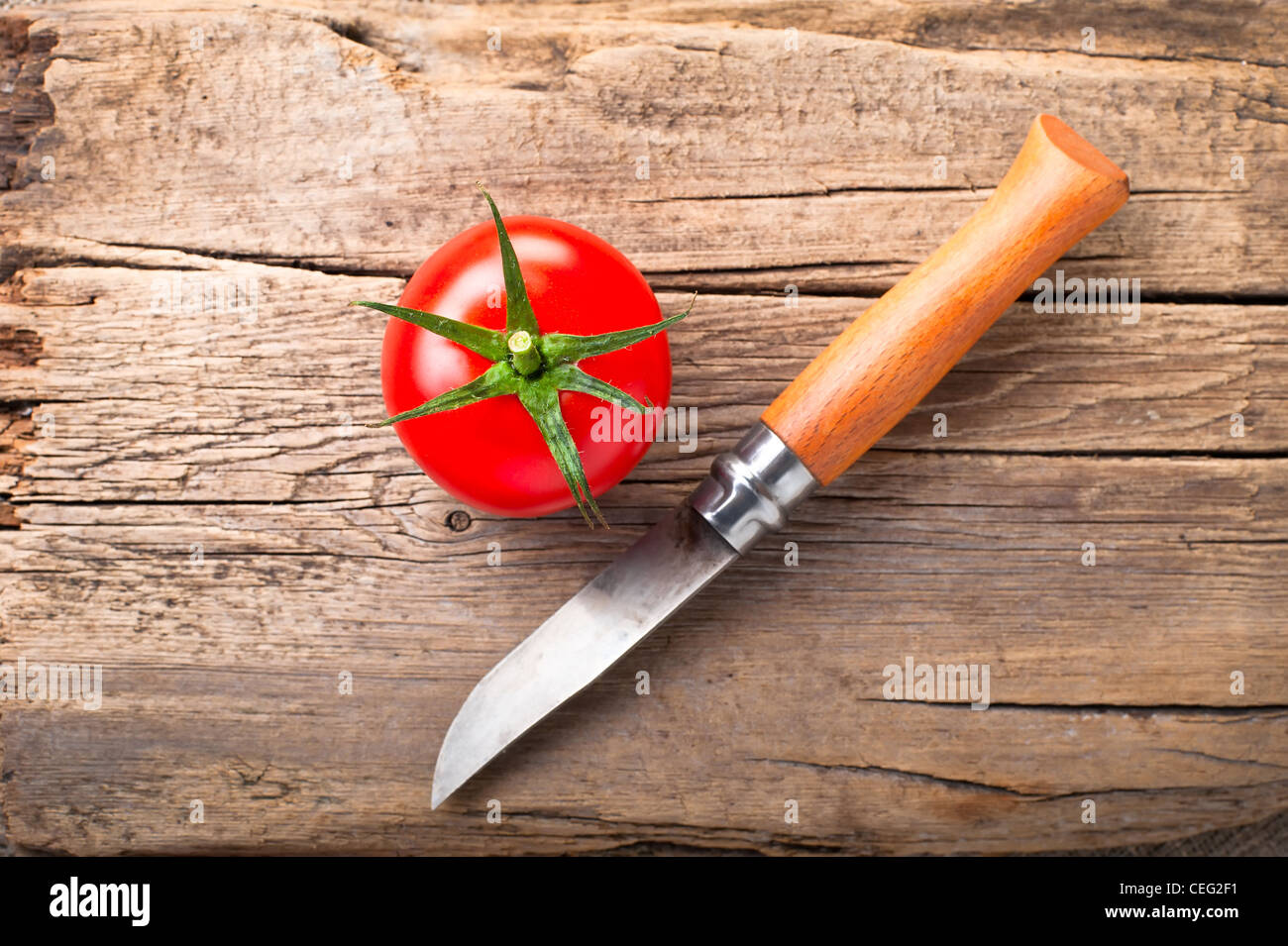 Fresh tomato and steel knife on vintage wooden cutting board Stock Photo