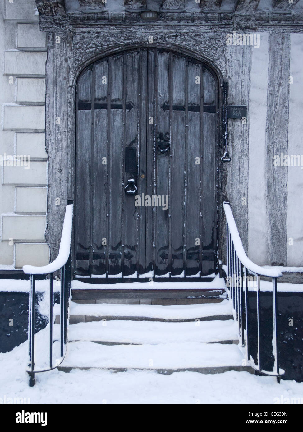 Snow-covered steps leading up to a closed old wooden arched door Stock Photo
