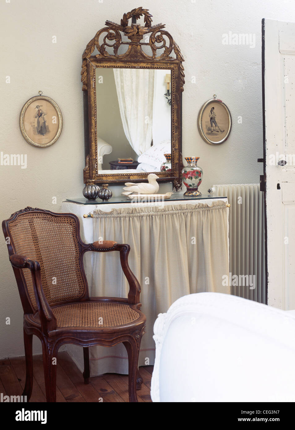 Antique ornate gilt mirror above dressing-table with cream drapes in  country bedroom with antique Bergere cane chair Stock Photo - Alamy
