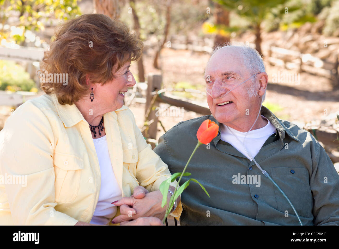 Senior Woman Outside with Seated Man Wearing Oxygen Tubes. Stock Photo