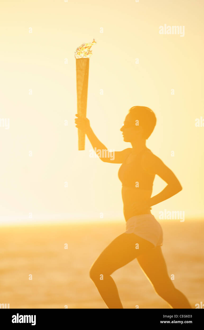 A woman running on the beach with a simulated olympics relay torch. Stock Photo