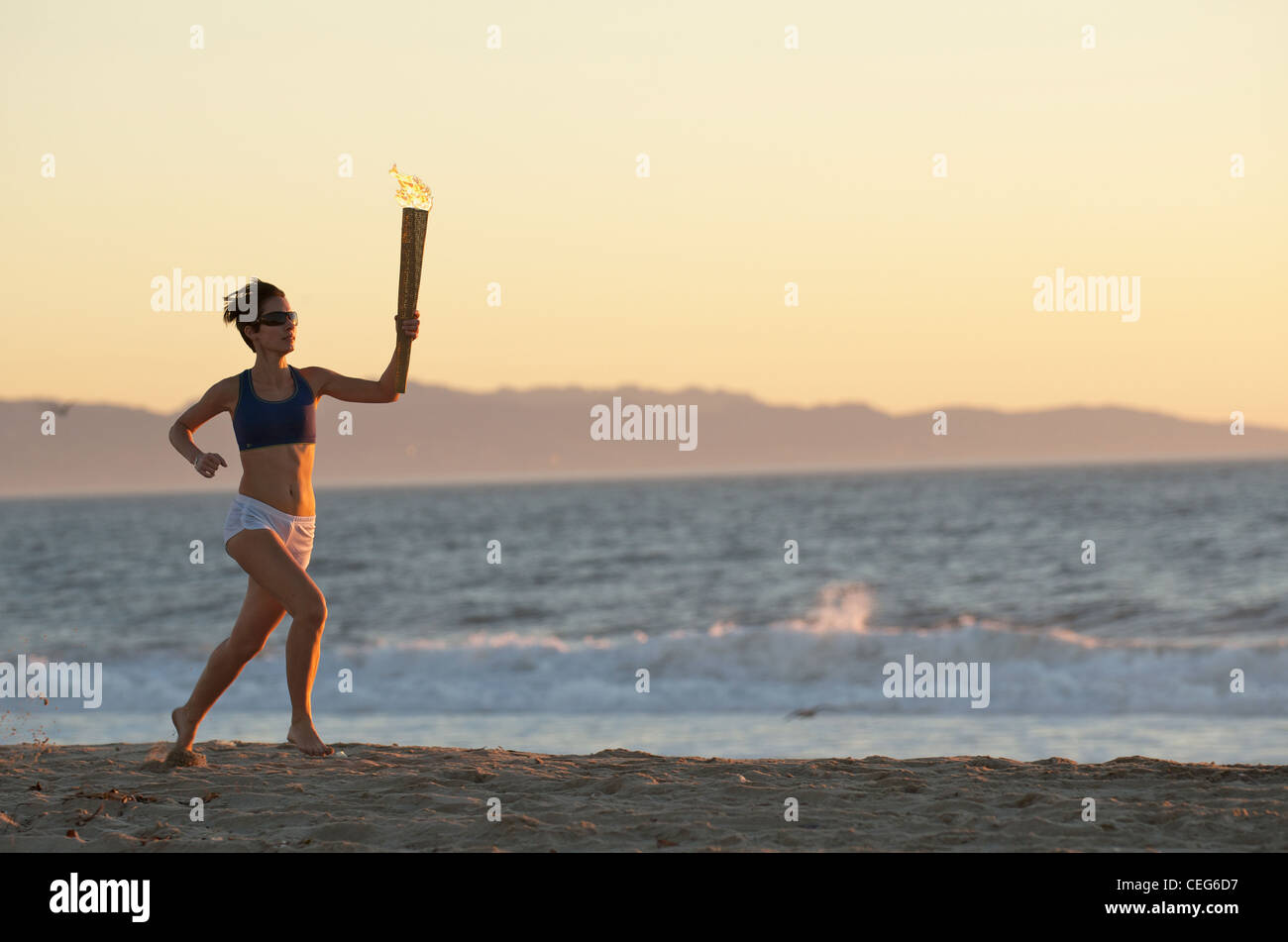 A woman running on the beach with a simulated olympics relay torch. Stock Photo