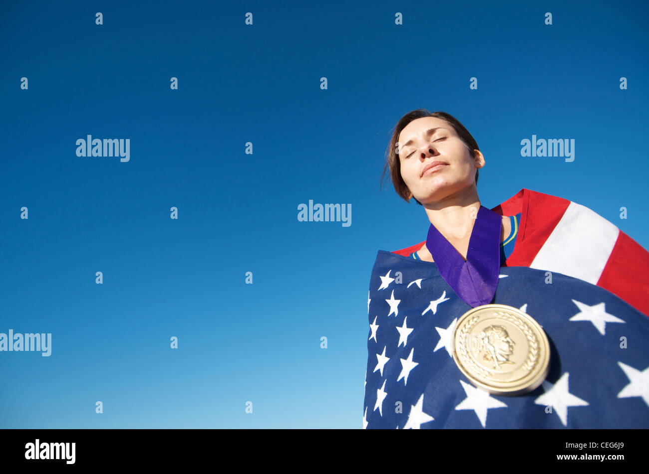 Portrait of a woman wrapped in an American flag wearing a simulated olympic gold medal. Stock Photo