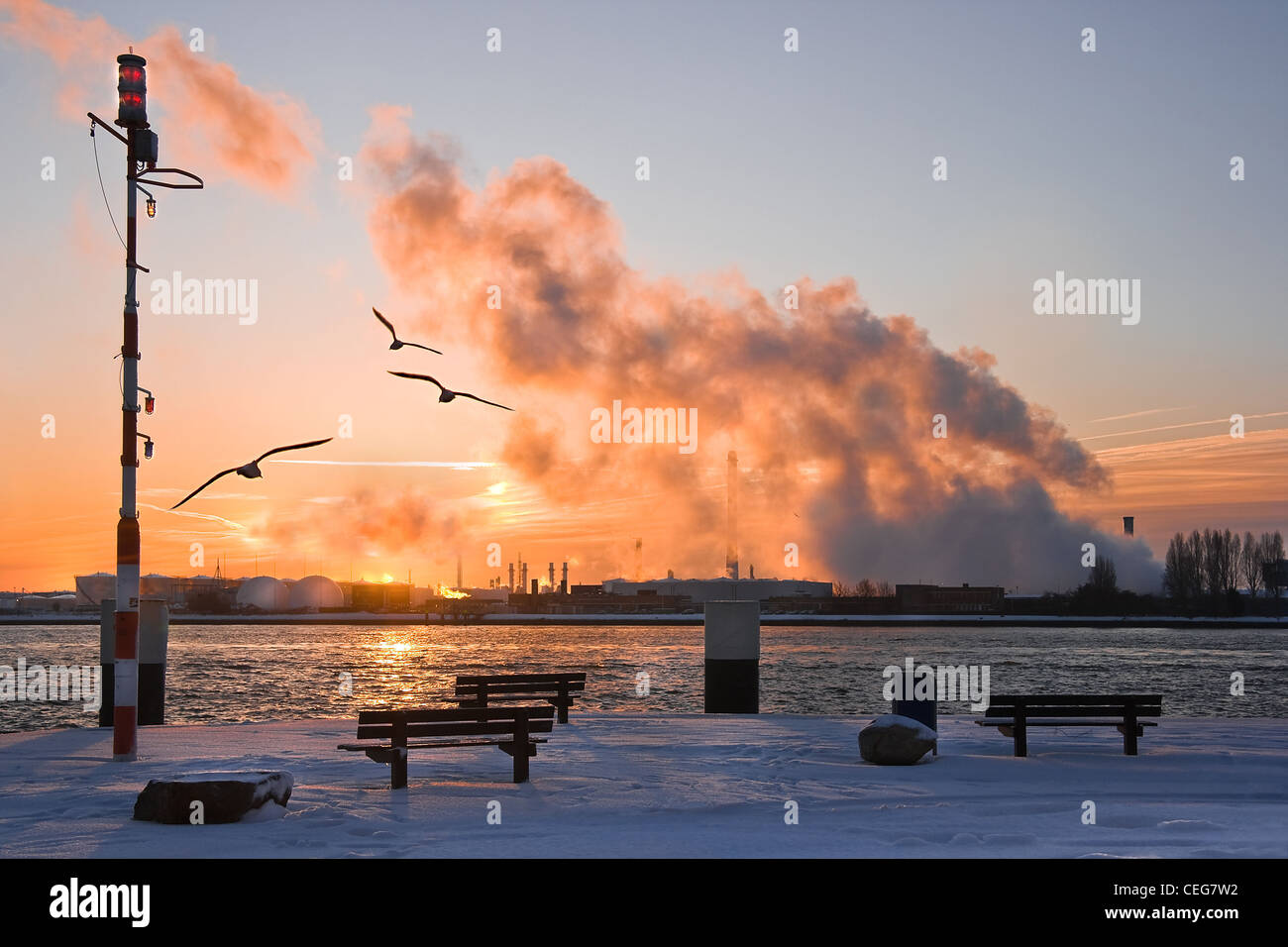 Industrial view at the riverside with snow, birds, smoke and pollution in winter at sunrise Stock Photo