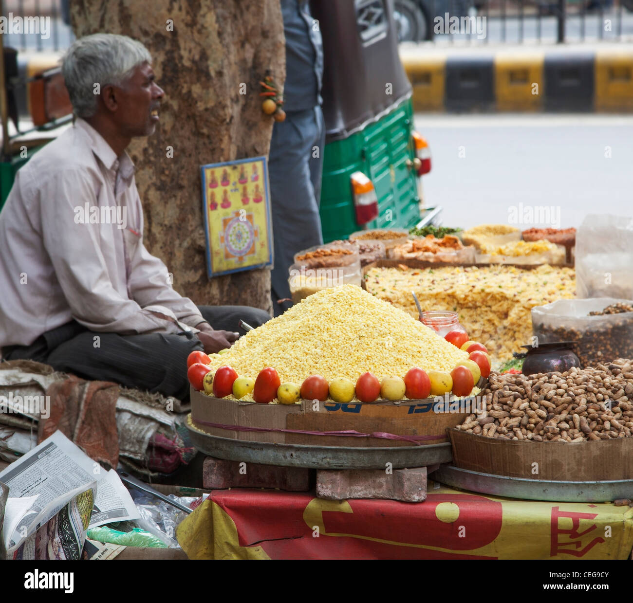 Bored-looking street seller selling rice, peanuts, fruit and other foods in New Delhi, India, arranged in a colorful display Stock Photo