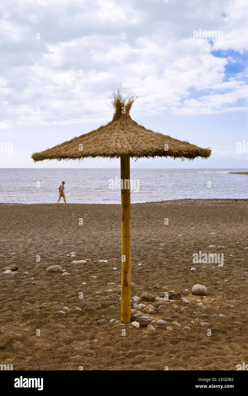 Deserted beach parasol with a lone person walking on the sand. Stock Photo