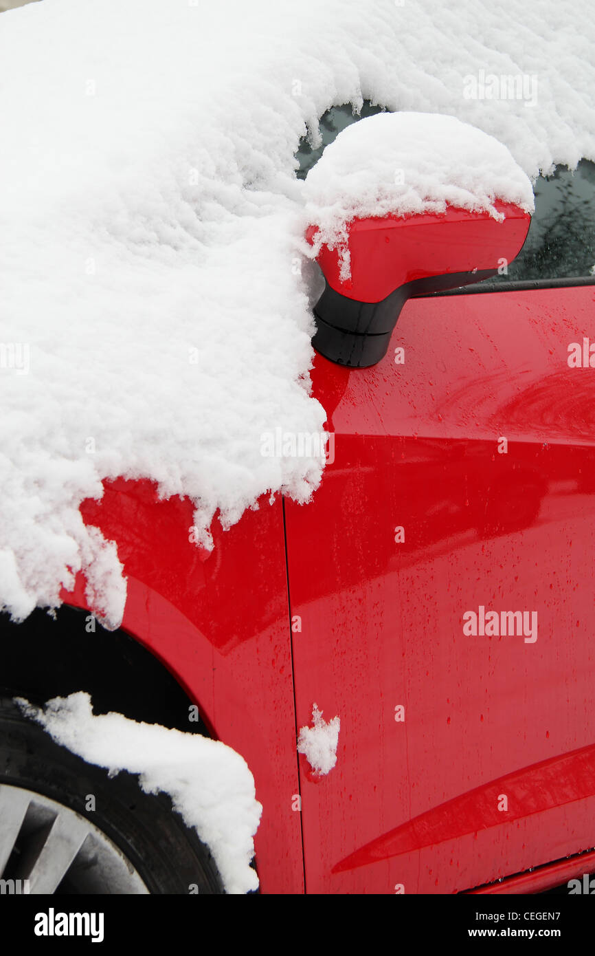 close up of side mirror and front wheel of red  car covered in snow. Taken from low angle. Stock Photo