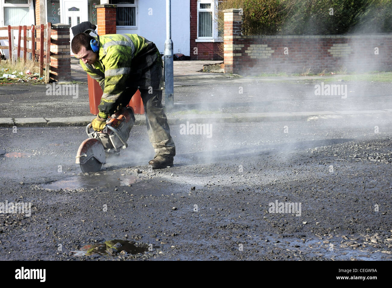 Workman and power saw with dust plume working on potholes Stock Photo