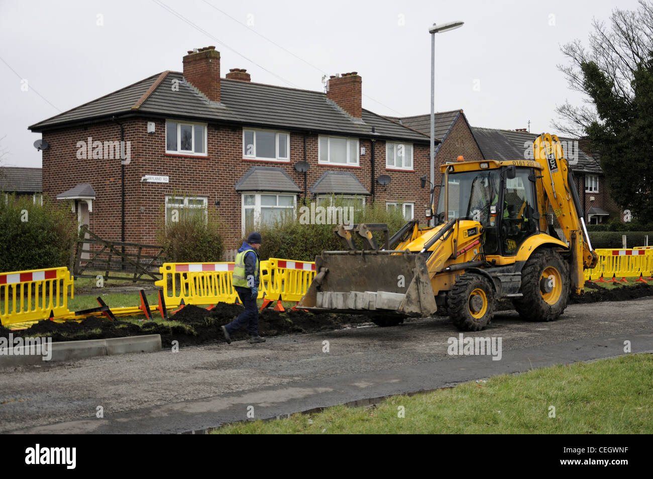 Yellow JCB and driver with kerb edgings in bucket  and workman laying them Stock Photo