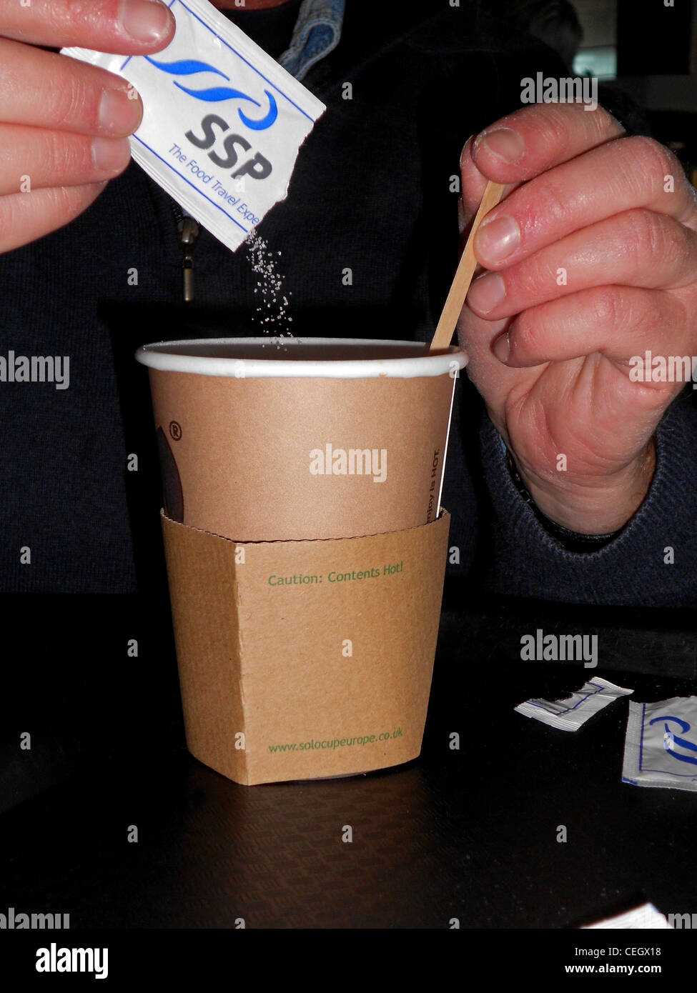 Man pouring sugar granules into cup of coffee, Terminal 3, Malaga Airport, Malaga, Costa del Sol, Andalucia, Spain. Stock Photo