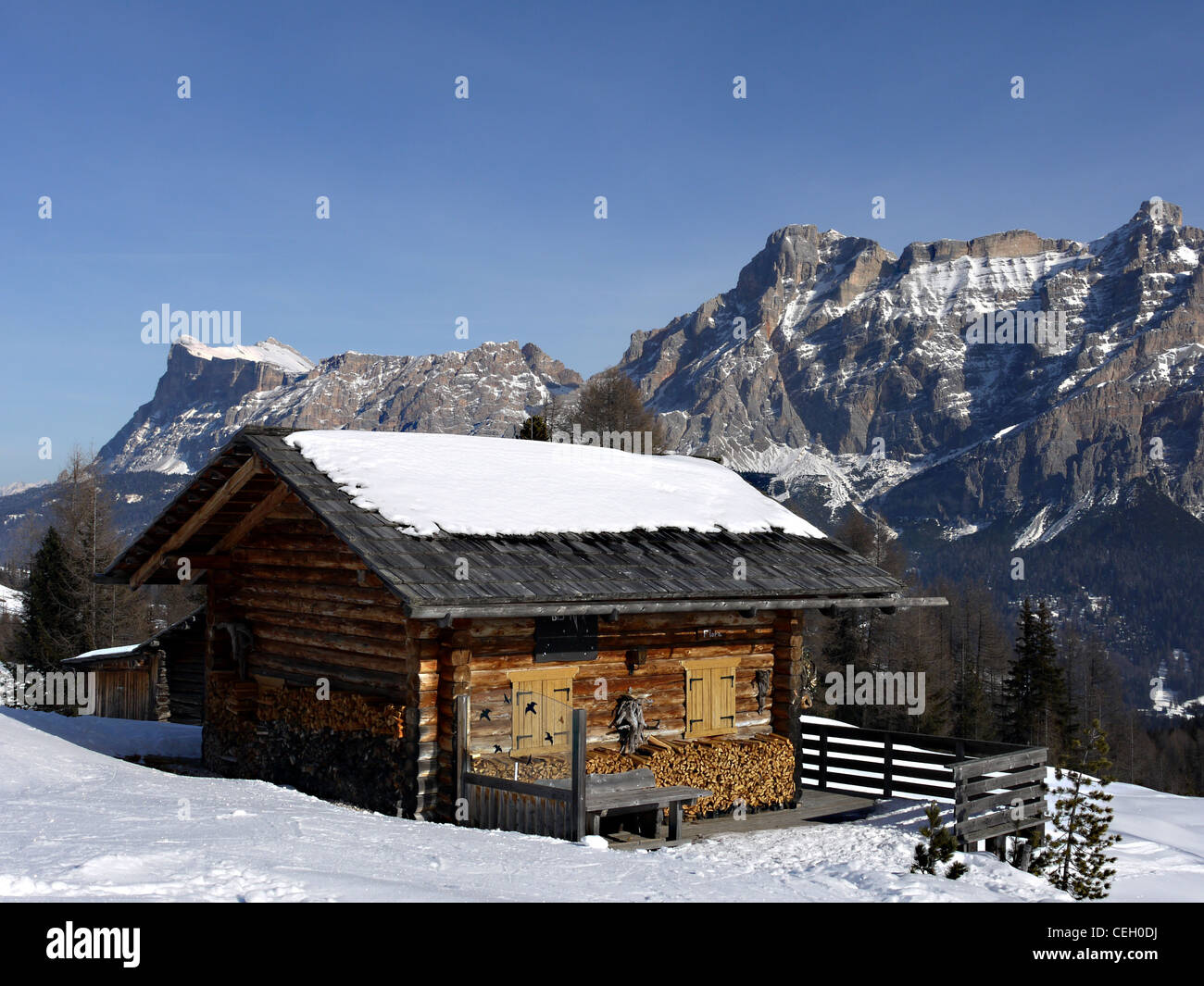 Wooden chalet in the snow near San Cassiano in the Dolomites in Italy. Mountains behind typical of area, called the Contarines. Stock Photo