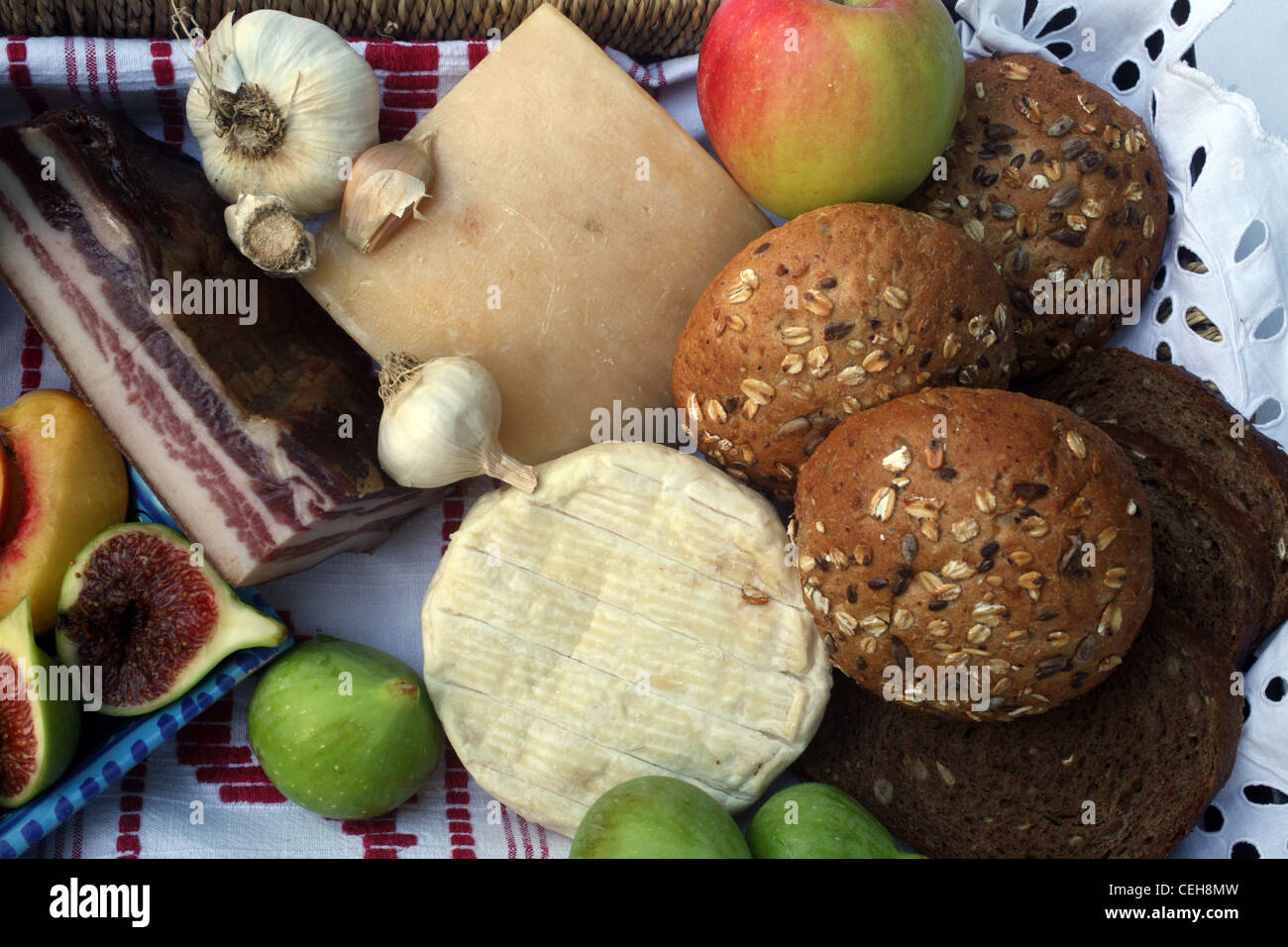 Rustic still life of bread, cheese, bacon and figs in a wicker basket Stock Photo